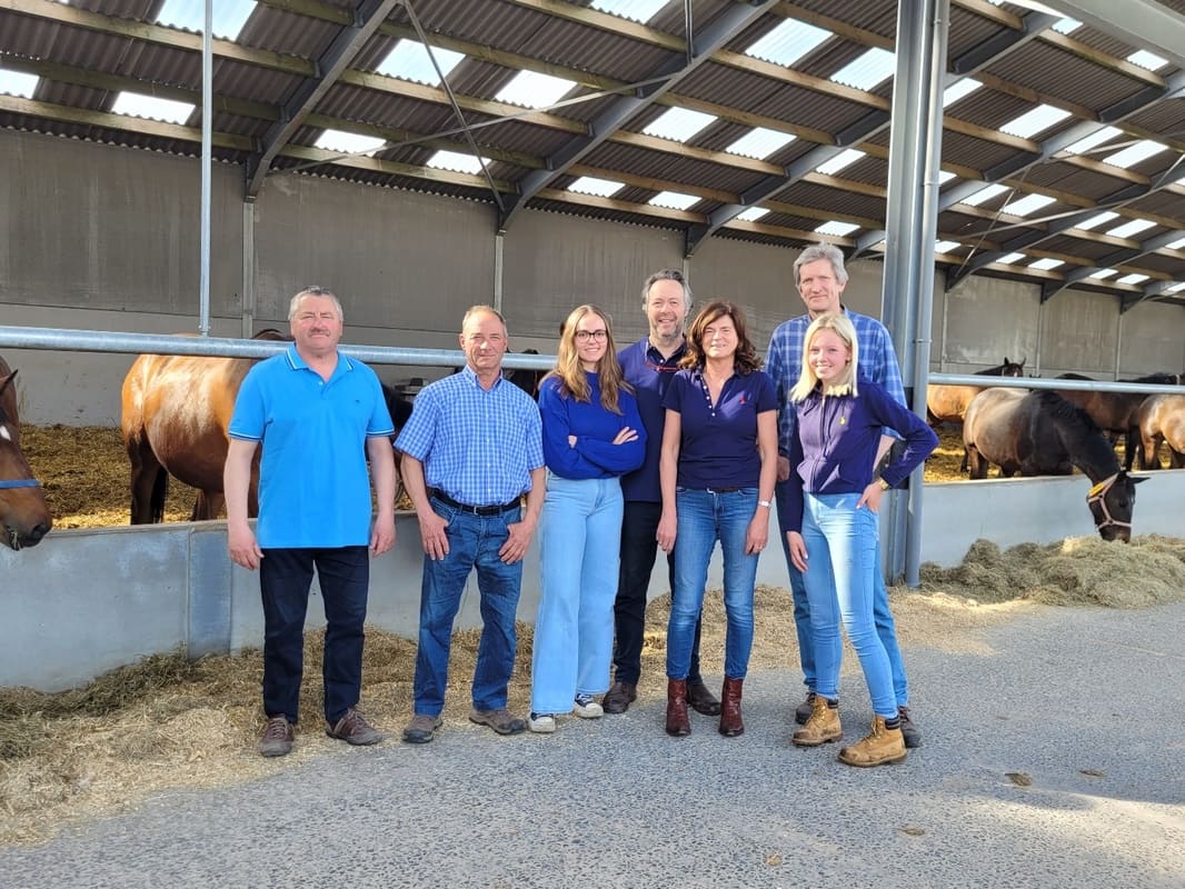 A group of people standing in front of a barn with horses.