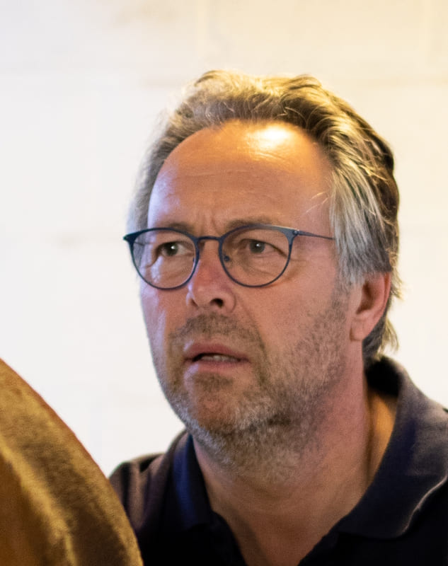 Man wearing glasses standing behind a horse in an examination box.
