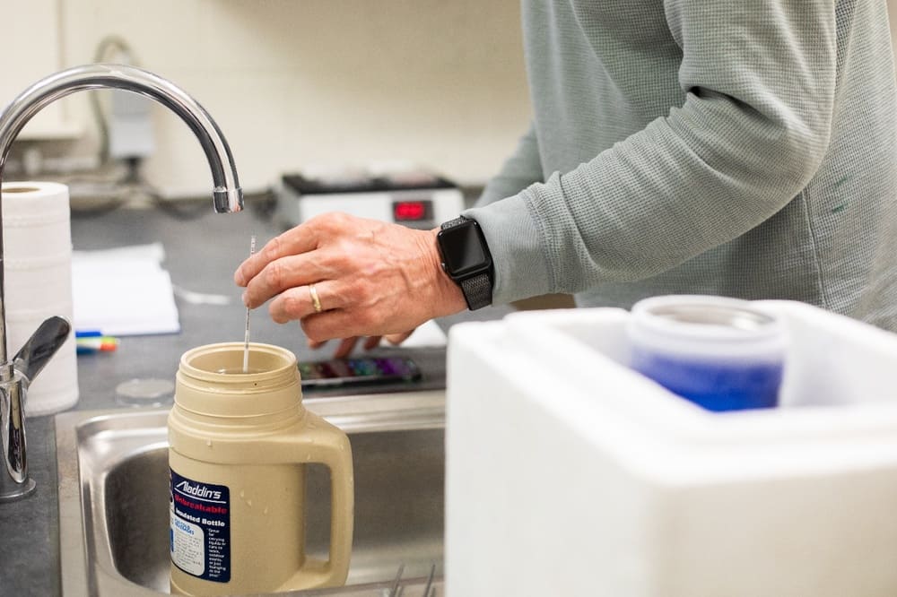 Un homme plonge une pipette dans un récipient thermos au-dessus d'un évier.